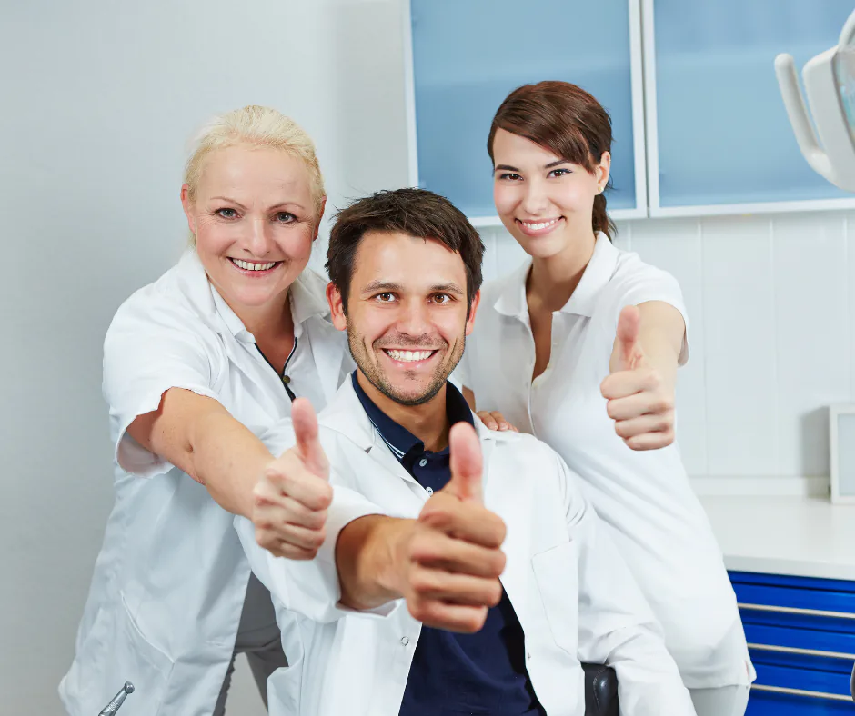 Tre professionisti sanitari in camice bianco sorridono facendo il gesto del pollice in su